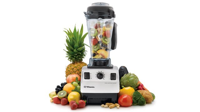 A Vitamix blender surrounded by fruits against a white background