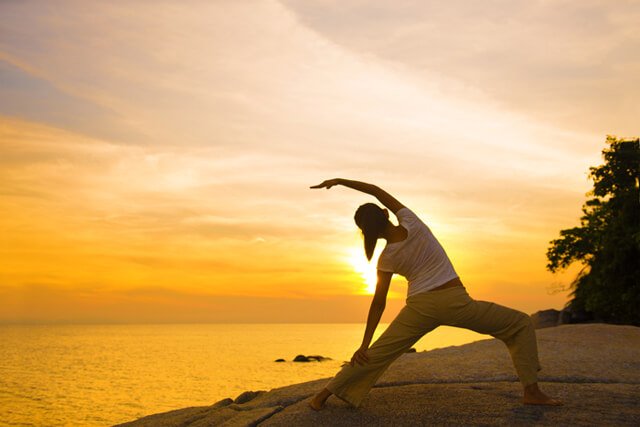 Woman in yoga pose at sunset overlooking the sea