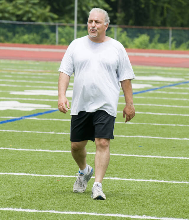 An overweight man walks on a football field