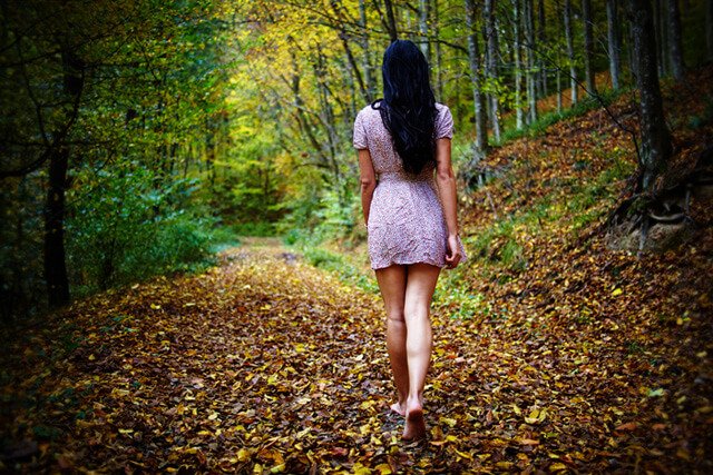 A woman walks barefoot in the woods in autumn