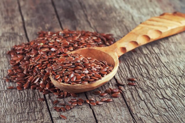 Flaxseed on a wooden spoon on a wooden surface