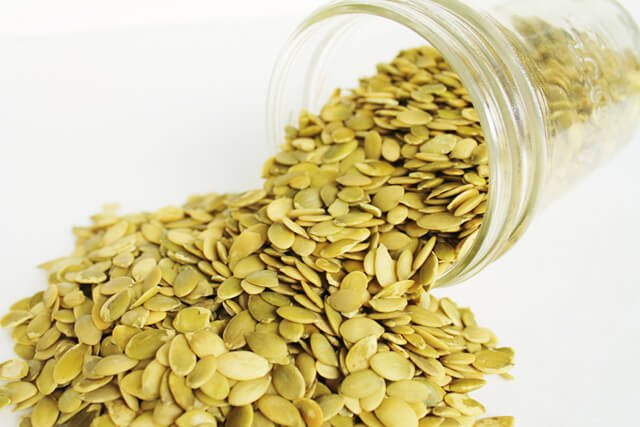 Pumpkin seeds spilling out of a jar against white background
