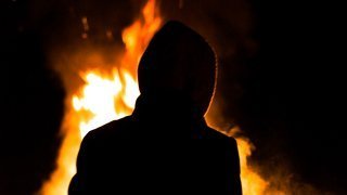 The back of a hooded man at a bonfire