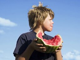A boy enjoys eating watermelon outdoors