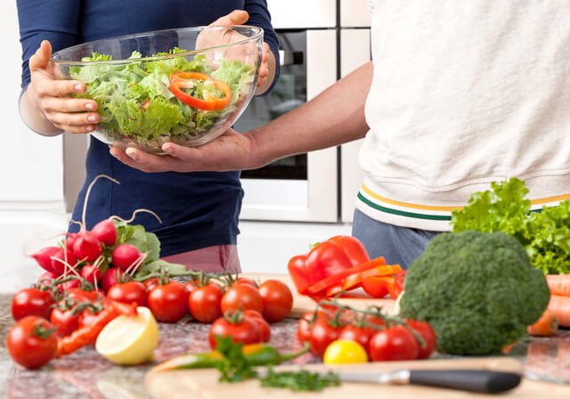 A man and woman make salad in a kitchen