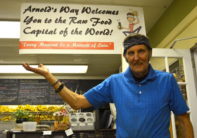 Arnold Kauffman with a sign saying "Arnold's Way Welcomes You to the Raw Food Capital of the World"