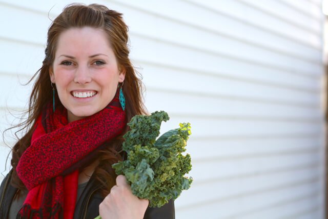 Ashley Clark holds a bunch of kale outside dressed in a winter coat