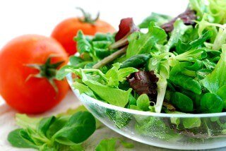Salad of baby greens with tomatoes against a white background