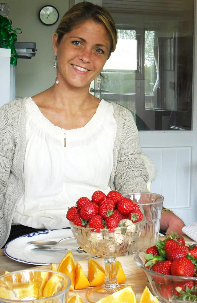 Louise Koch smiles behind a bowl of strawberries on a table