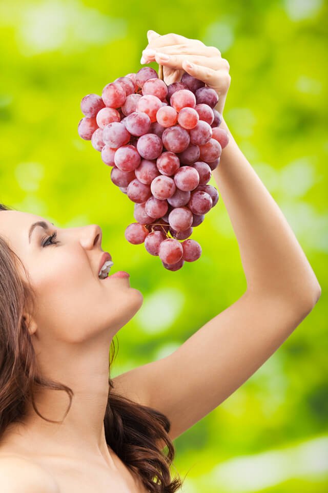 A woman playfully eats grapes outdoors