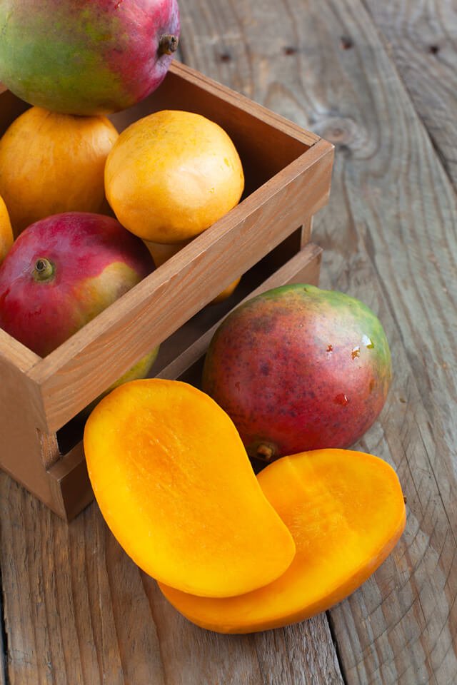 Whole and cut mangoes in a basket on wood