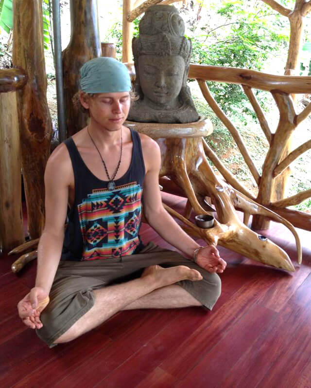 Evan Rock meditates beside a statue on a wooden floor