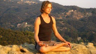 Evan Rock meditates in a hilly region