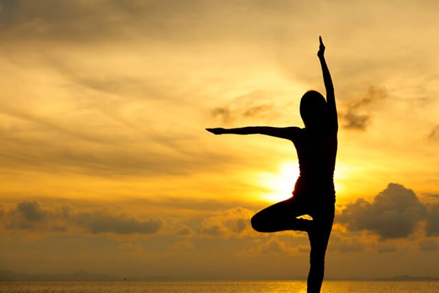 Silhouette of a woman practicing yoga by the sea at sunset