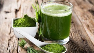 A small glass of barley grass juice with powder and grass blades