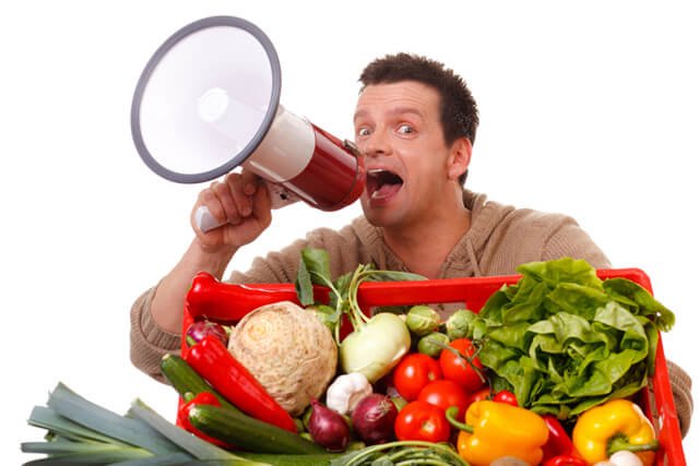 A man speaks into a megaphone adjacent to fruits and vegetables in a large basket