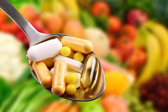 A spoonful of supplements with fruits and vegetables in the background