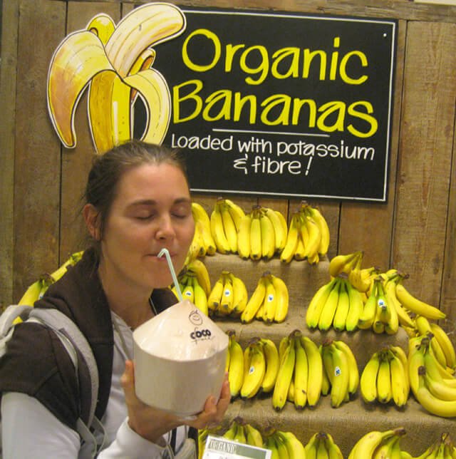 Reny Kattel sips coconut water from a straw beside an organic banana stand