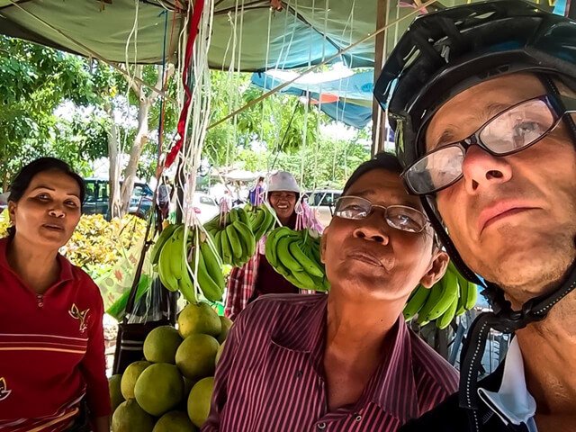 Mark Tassi photographs himself and two others at a fruit market in Cambodia