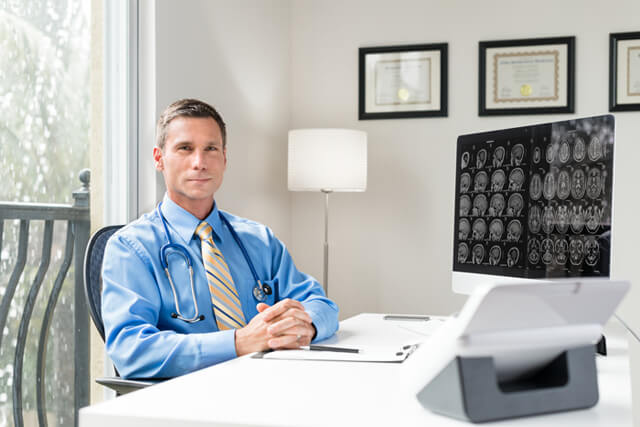 A doctor sits behind a desk in an office