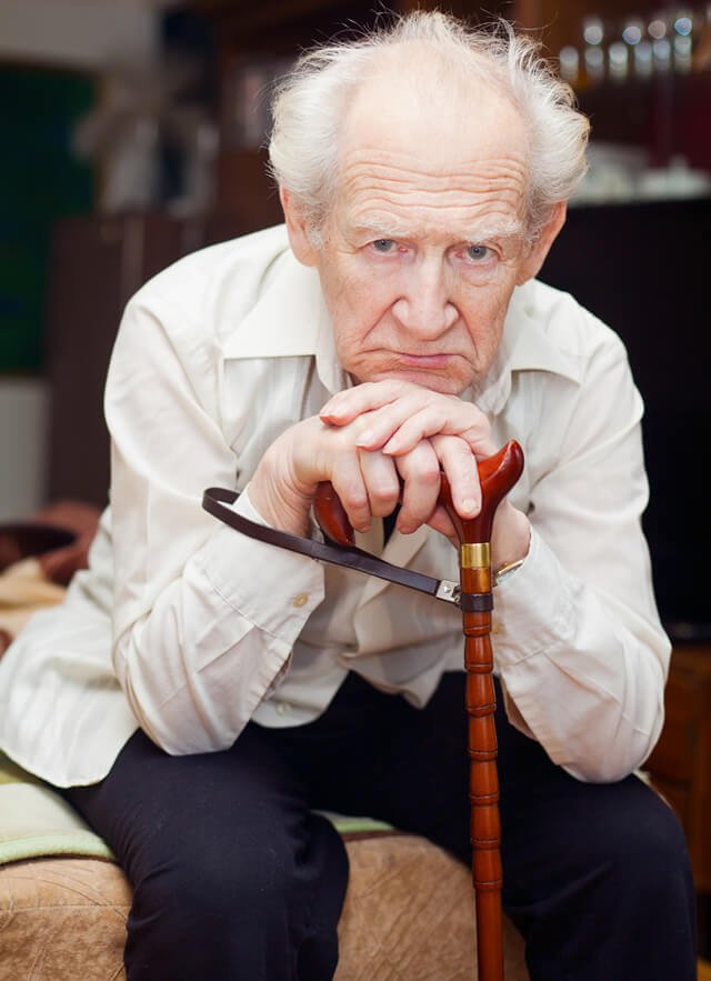 Unhappy old man leers while hunched over a cane