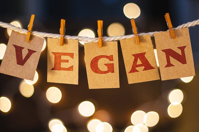 The word "vegan" printed on clothespin-clipped cards in front of defocused glowing lights