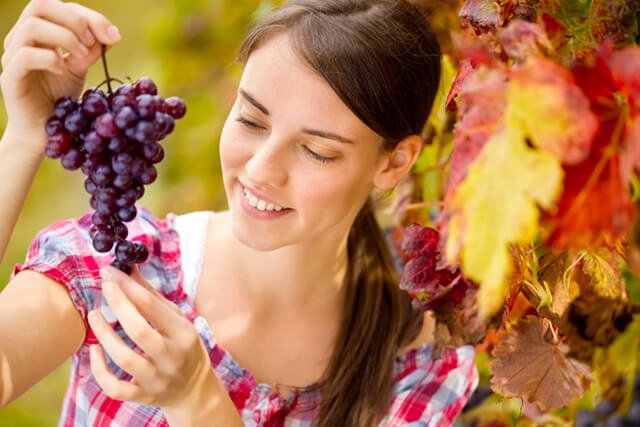 Cheerful young woman looking at bunch of red grapes