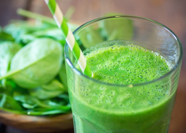 A spinach green smoothie with a green-and-white straw