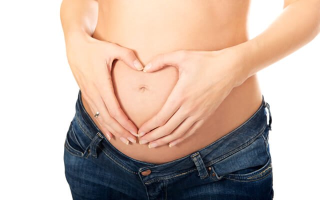 Fit pregnant woman making heart shape on belly