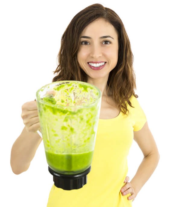 A woman holds a blender container of green smoothie