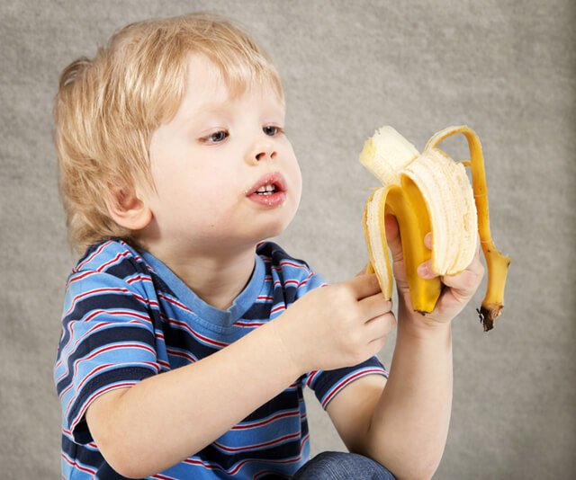 A young boy eats a banana