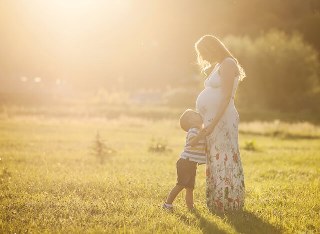 Small boy kissing belly of his pregnant mother outdoors