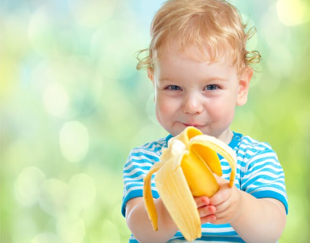 A male toddler eats a banana
