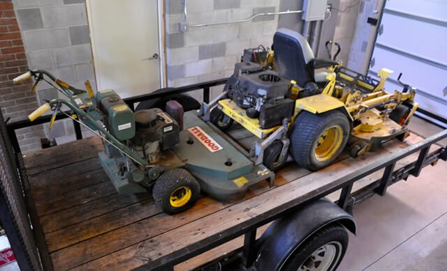 Two lawnmowers are stationed on a trailer