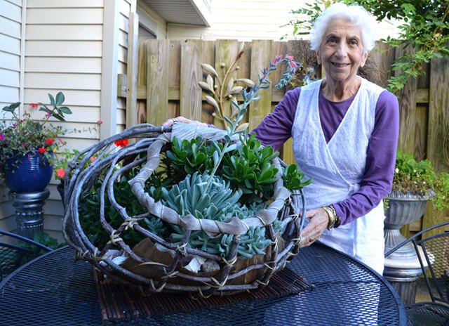 Betty Korba stands beside a plant arrangement outside her home