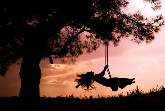 Silhouette of a young woman on a swing with sunset background