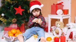 A boy peels an orange next to a Christmas tree