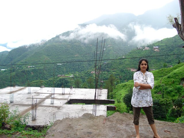 Rupinder Kaur stands with arms folded at the foot of a mountain