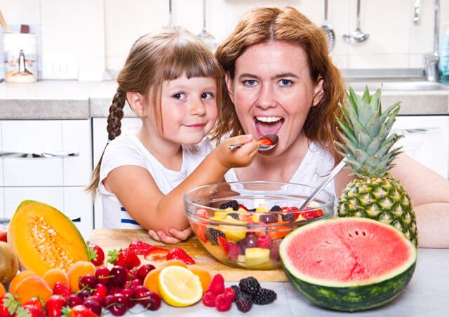 Daughter feeds mother from a bowl of fruits