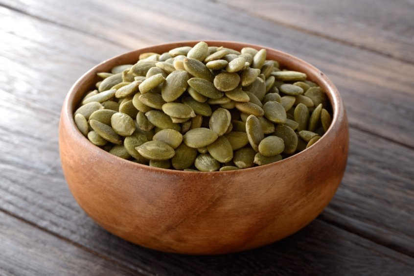 Pumpkin seeds in a wooden bowl on a table - Fruit-Powered