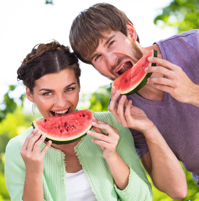 A woman and man eat watermelon slices outside