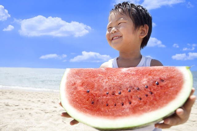 Asian boy eats watermelon on a beach