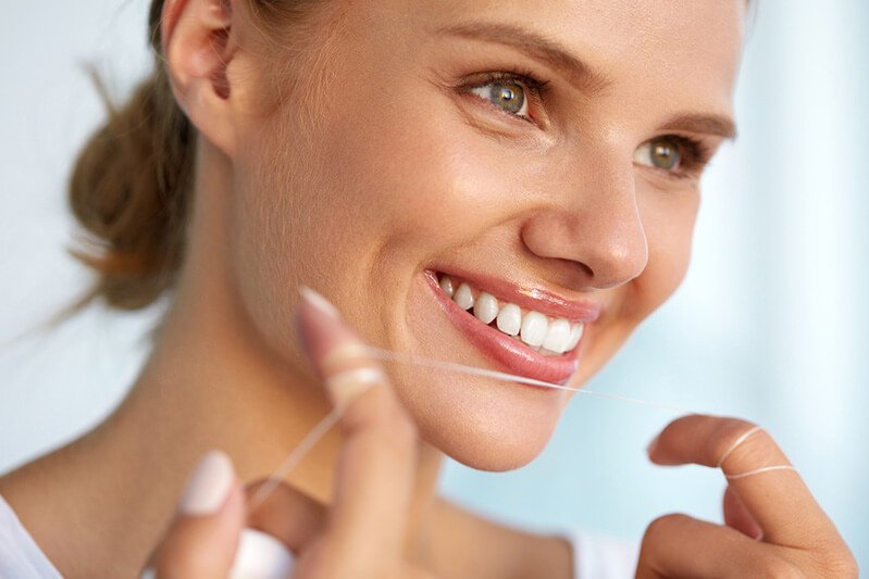 A woman flosses her teeth, demonstrating oral hygiene care