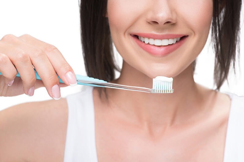 Woman holds a toothbrush topped with toothpaste, practicing oral hygiene care