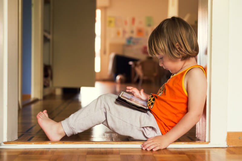 Child plays with a tablet and leans against a wall, exhibiting poor posture