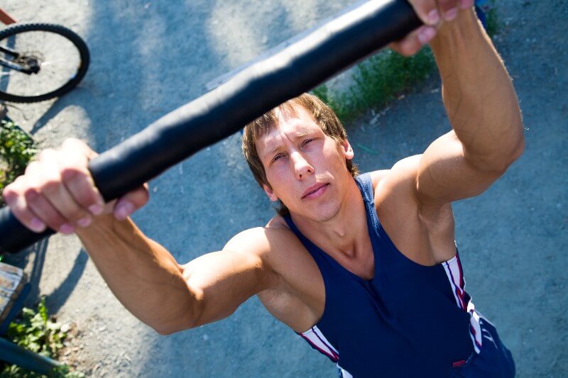 A man does pull-ups on a bar outside
