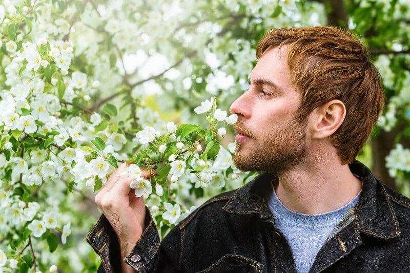 A man smells a flower on a tree
