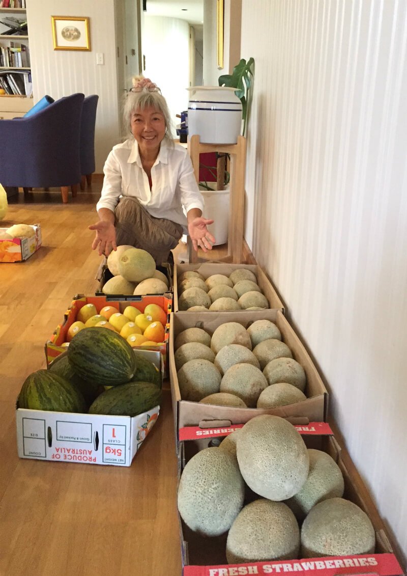 Ping Chan crouches beside dozens of melons