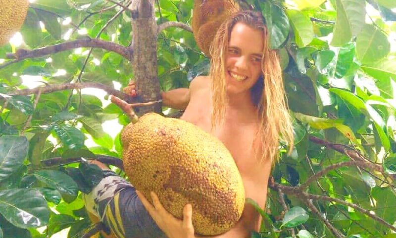 Nicolas Dudet carries a jackfruit while hanging from a tree