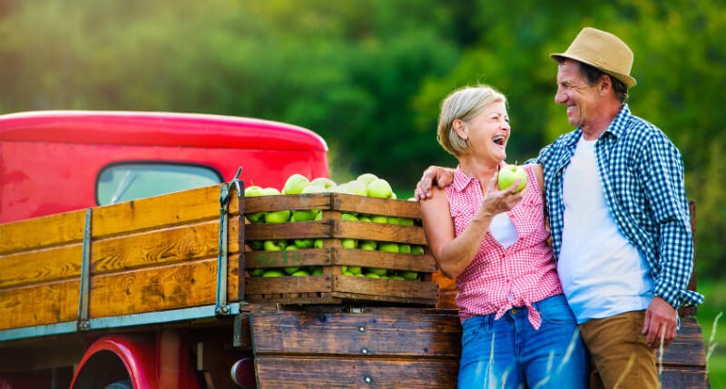 A woman enjoys freshly picked apples with a man beside a truck 